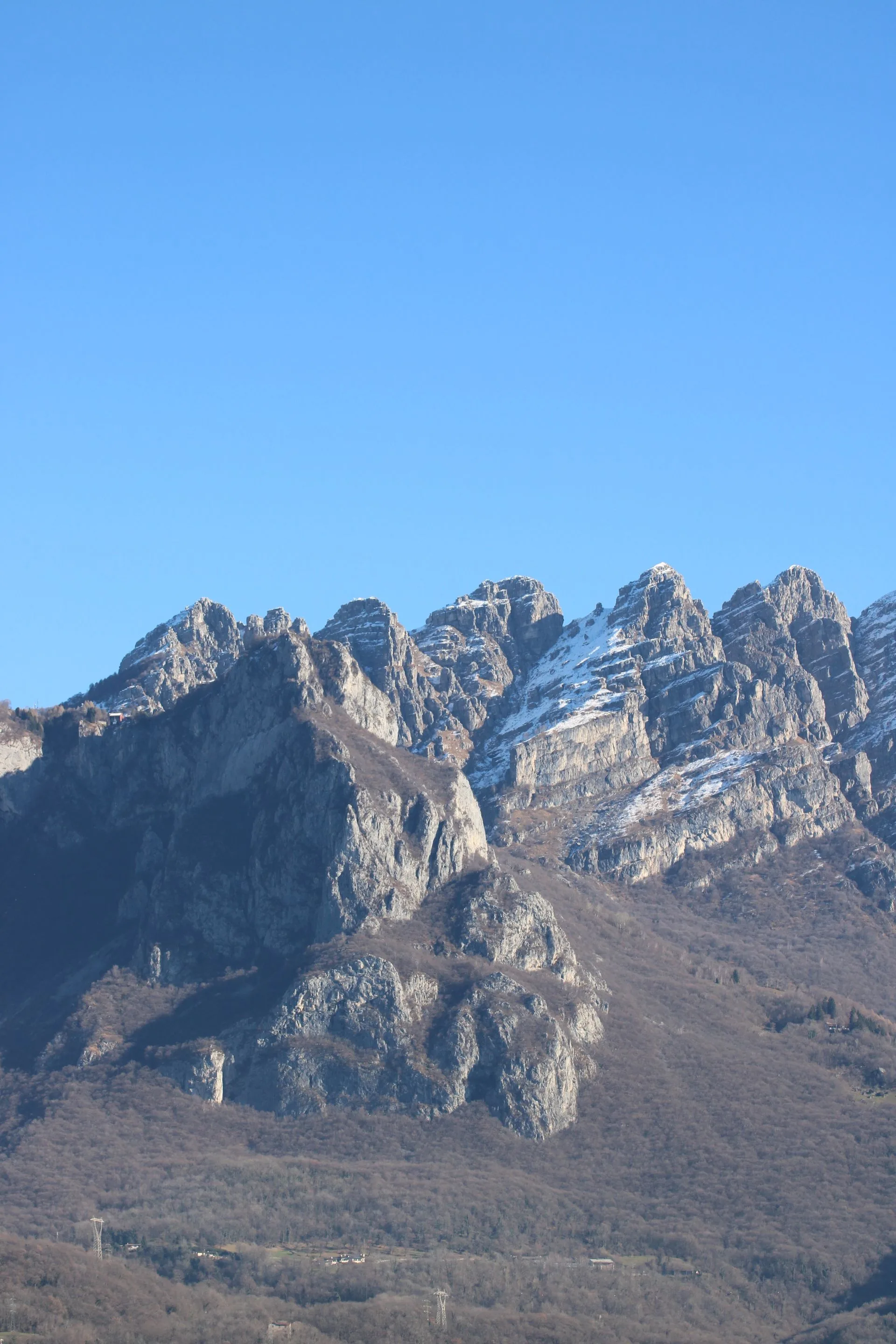 A stunning view of the snow-capped Grigna mountains under a clear blue sky in Lombardy, Italy.